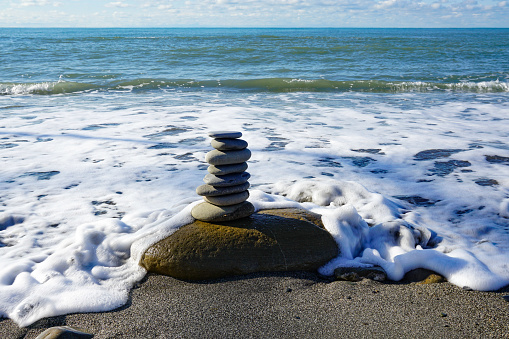 Turret of sea pebbles on the surf line against the backdrop of a calm sea and horizon