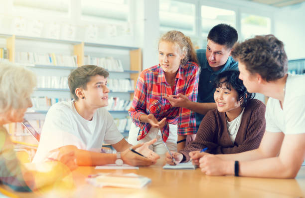 istock Positive teenage students working and discussing in groups in library 1441905076