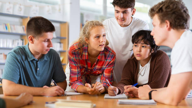 istock Group of schoolchildren in the school library, discussing something 1441905077