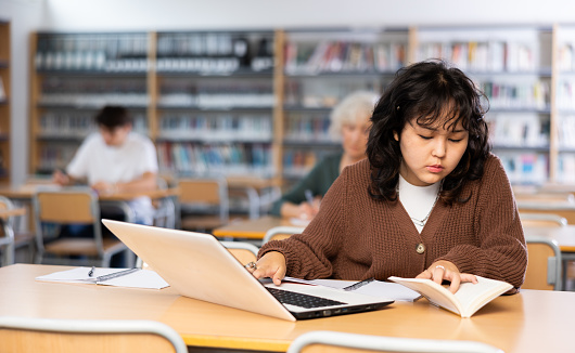 Asian teenager girl with a laptop studying in the school library
