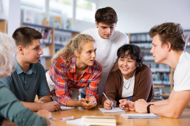 istock Group of positive young teen students communicating in library, talking and making notes 1441907279