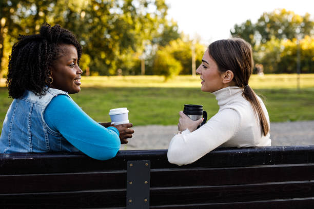 Two girlfriends having coffee, chatting and bonding while enjoying a sunny day outside