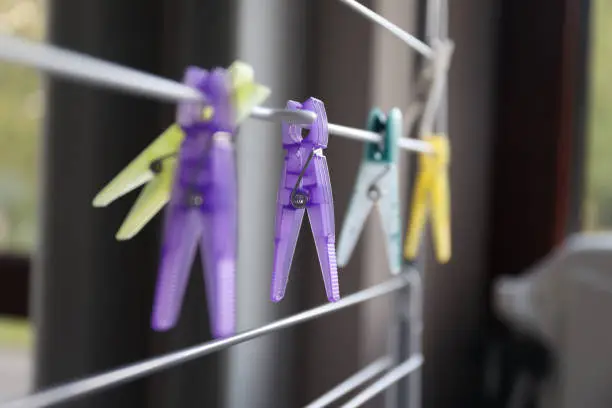 Photo of a portrait of a purple washingpin hanging on a washing rack inbetween other colorful laundry clamps or pens. they are used to hang and dry clothing on a rack or line indoors or outdoors.