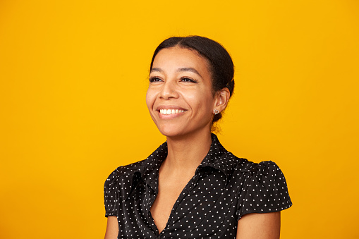 Close up studio portrait of cheerful middle aged afro american woman in polka dot blouse against a yellow background
