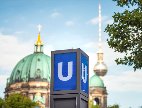 A sign for a U-Bahn Subway station near Berliner Dom, with the cathedral and the city's TV Tower in the background.