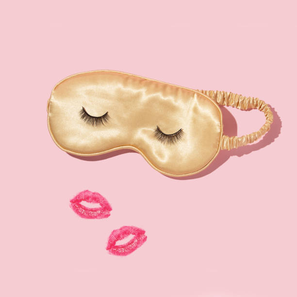 Creative layout with yellow sleep mask with false eyelashes  and kiss prints on pastel pink background. 80s or 90s retro fashion aesthetic concept. Minimal romantic cosmetic beauty Valentines day idea.
