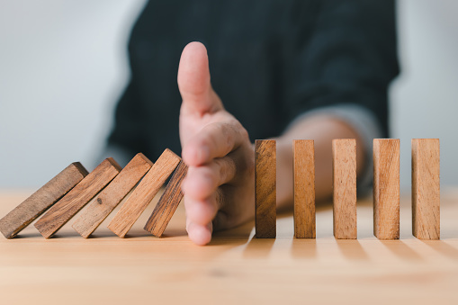 Business Risk and Strategy: Hand stopping the wooden block domino effect of a business crisis or risk protection concept, prevention, and development to stability