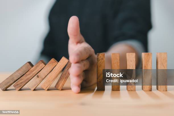 Business Risk And Strategy Hand Stopping The Wooden Block Domino Effect Of A Business Crisis Or Risk Protection Concept Prevention And Development To Stability Stock Photo - Download Image Now