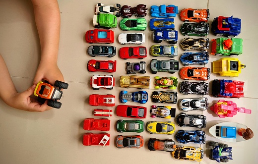 This is a nostalgic image of a young boy playing with an antique toy SUV on a wood floor.