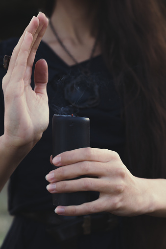 Close up extinct black candle concept photo. Withcy dressed woman. Front view photography with female hands on background. High quality picture for wallpaper, travel blog, magazine, article