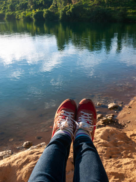 a pair of red sneakers legs in a pair of red sneakers on the hill reaching to the lake lake kivu stock pictures, royalty-free photos & images