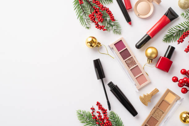 クリスマスショッピングのコンセプト。白い背景に装飾的な化粧品のトップビュー写真リップグロスマニキュアマスカラアイシャドウパレット金色のつまらないもの松の枝ヤドリギとコピー�