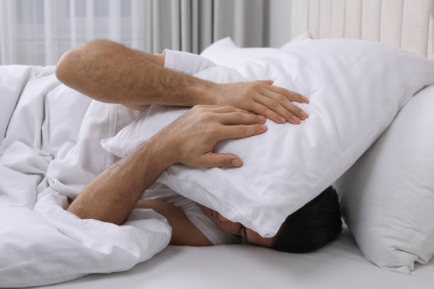 istock Handsome man sleeping under pillow in bed at home 1441920114