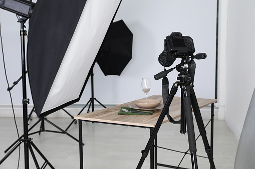 Table with stylish dinnerware in front of camera and professional lighting equipment indoors. Photo studio set