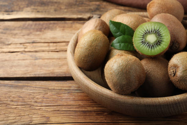 istock Bowl with cut and whole fresh kiwis on wooden table, closeup. Space for text 1441920247