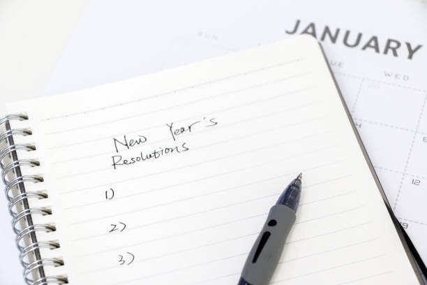 escribir resoluciones de año nuevo, lista en el bloc de notas con bolígrafo, calendario de enero en el fondo, enfoque selectivo. establecer metas para el nuevo año. - propósito de año nuevo fotografías e imágenes de stock