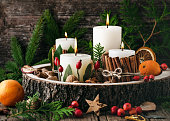 Christmas, advent wreath with four white burning candles decorated with natural material. Slices of fresh dried apple, orange and spices for cooking or baking.