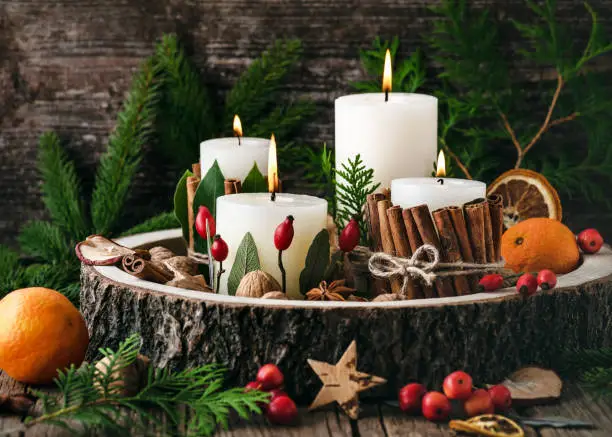 Christmas, advent wreath with four white burning candles decorated with natural material. Slices of fresh dried apple, orange and spices for cooking or baking. Rustic style. Handmade home decoration.