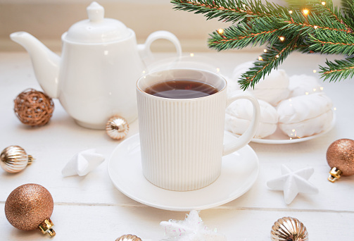 Winter, Christmas, New Year decoration composition, concept, background. White Mug, cup of hot tea, coffee, meringue, knitted plaid. Christmas lights. Christmas mood morning. Xmas greeting card.