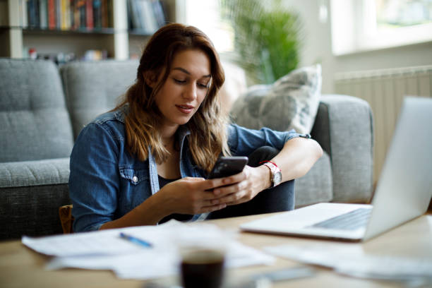 istock Young smiling woman using mobile phone while studying at home 1441924671
