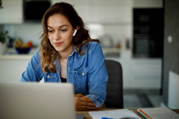 Smiling young woman with bluetooth headphones attends an online course at home stock photo