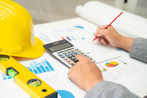 istock Asian engineer with architectural house plan project blueprint, graph and yellow helmet and engineering construction tools. 1441925028