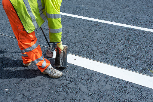 Road workers applying hot melt traffic resistant paint for white, yellow and red road marking lines on new build asphalt road