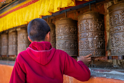Novice Tibetan buddhist monks turning the prayer wheels, Tsarang village in Upper Mustang. Tsarang monastery on the background. Mustang region is the former Kingdom of Lo and now part of Nepal,  in the north-central part of that country, bordering the People's Republic of China on the Tibetan plateau between the Nepalese provinces of Dolpo and Manang.
