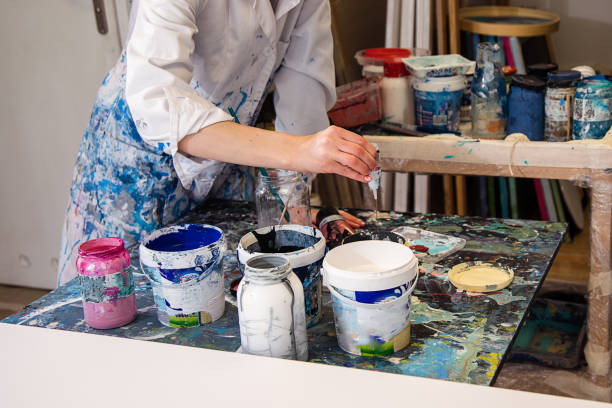 istock Close up of painter hands squeezing paint from tube on table wearing white coat covered with splashes of paint 1441931258