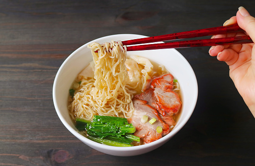 Hand Gripping Delectable Chinese Roasted Pork Egg Noodles with Chopsticks