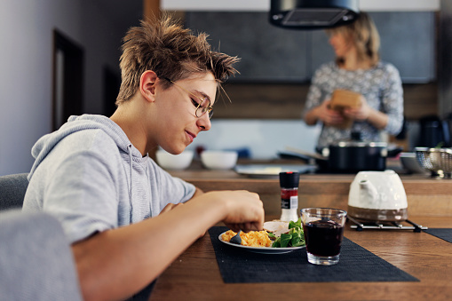 Teenage boy having scrambled eggs for breakfast. Mother is visible in t he kitchen.
Shot with Canon R5
