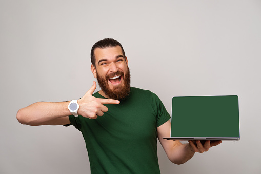 Look here at this screen and offer where points a bearded smiling man. Studio shot over grey background.