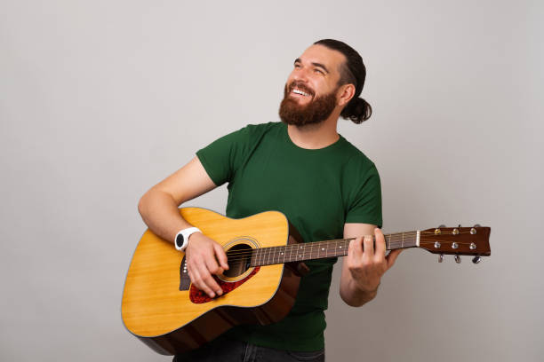 istock Handsome strong man is playing an acoustic guitar while looking up and smiling. 1441941247
