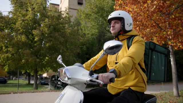 Delivery person driving Vespa through city, delivering orders during day