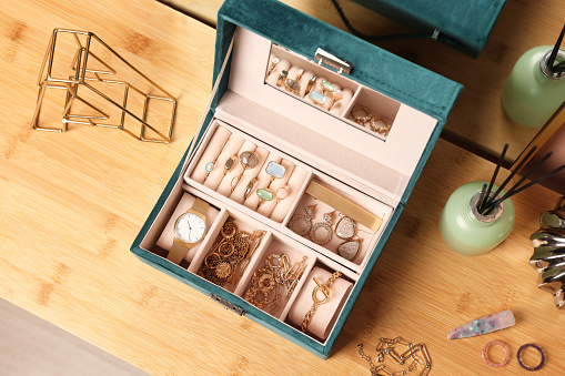 Elegant jewelry box with beautiful bijouterie and expensive wristwatch on wooden table, top view