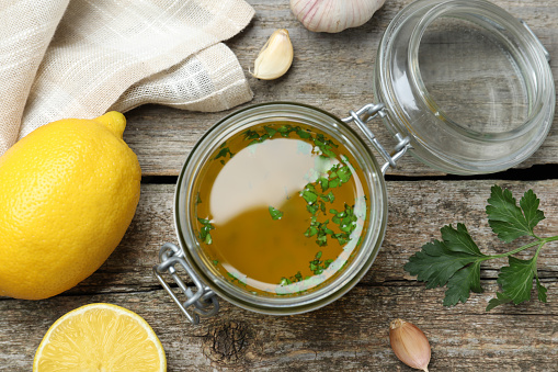 Jar with lemon sauce and ingredients on wooden table, flat lay. Delicious salad dressing