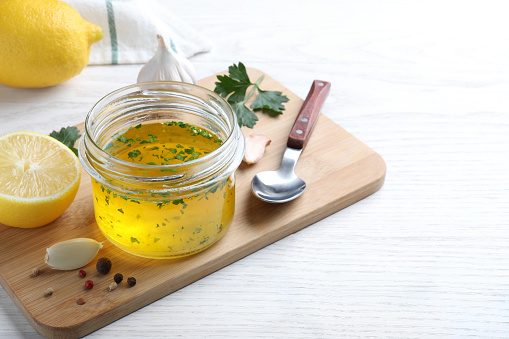 Jar with lemon sauce and ingredients on white wooden table, space for text. Delicious salad dressing