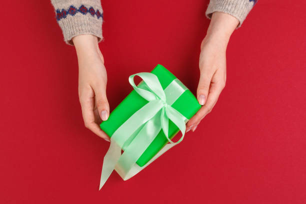 istock Female hands with christmas gift on red background, top view, copy space 1441950516