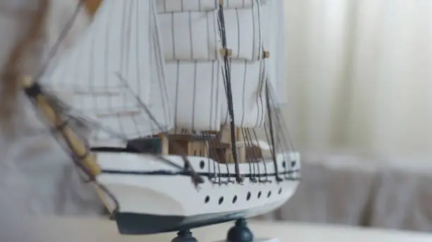 Close-up of the little marine white ship model from the wood on a striped background on the blurred light background. Hobby and collecting concept