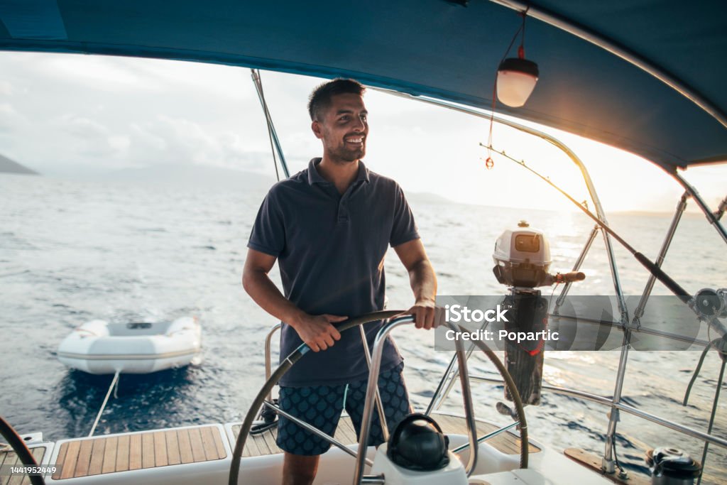 Young man enjoy sailing Smiling young man as helmsman on sailboat. Nautical Vessel Stock Photo