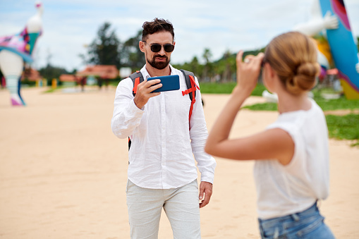 Man taking photo of girlfriend on smartphone when they are walking in amusement park