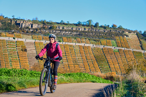 nice senior woman riding her electric mountain bike in the steep autumnal colored vineyards of River Neckar Valley,Baden-Wuerttemberg, Germany