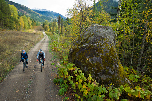 Two men go past a large rock during a gravel bicycle ride in October. Gravel bikes are similar to road bikes but have oversized tires for riding on rough terrain.