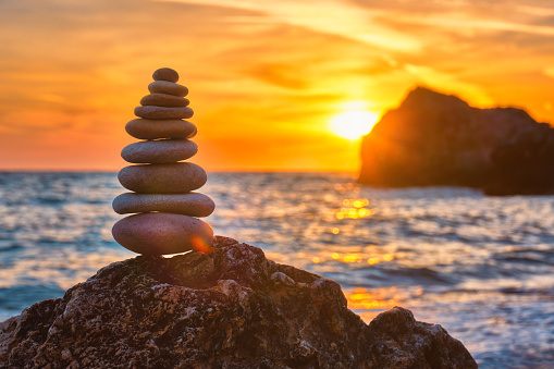 Concept of balance and harmony. Cairn stack of stones pebbles cairn on the beach coast of the sea in the nature on sunset. Meditative art of stone stacking