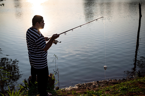 Portrait of a young Latin man fishing at a lake in a public park, in the late afternoon.