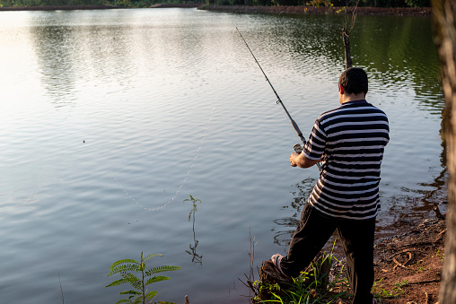 Portrait of a young Latin man fishing at a lake in a public park, in the late afternoon.
