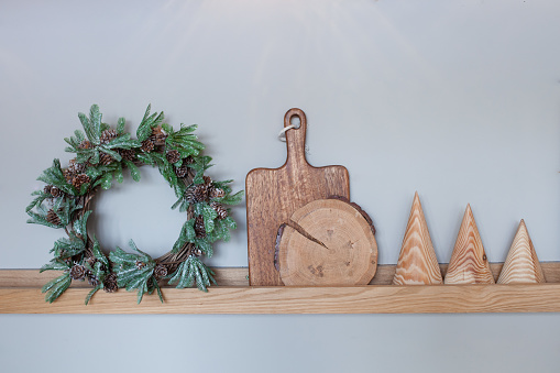 Details of modern christmas kitchen interior. Christmas wreath, wooden cutting board, round stand and decorative wooden cones on a gray wall background. Home improvement. Selective focus.