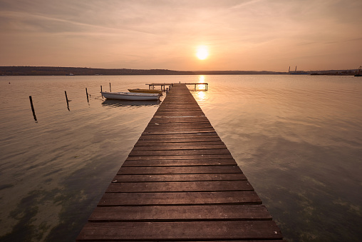 Landscape photo of a wooden jetty and two boats on lake at sunset in Varna, Bulgaria.