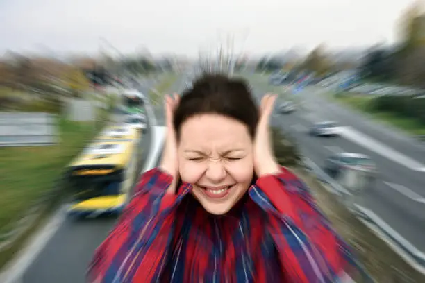 Photo of Woman covering her ears in the street while vehicles are passing by fast