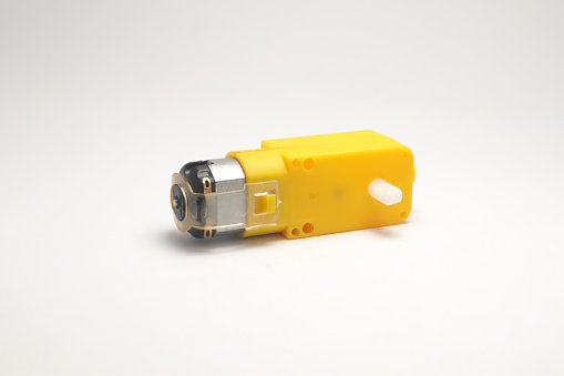 A DC motor with its power socket equipped with a yellow gearbox side view on a white background. DIY materials for the electronics hobbyist.